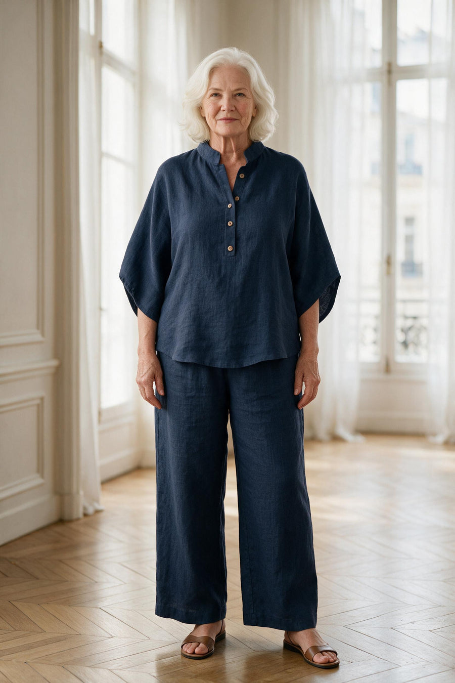 Femme de 70 ans portant l'ensemble Clarisse en lin bleu marine, tunique à col montant et pantalon large, dans un appartement parisien