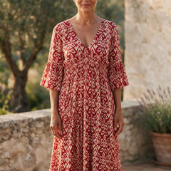 Femme de 64 ans portant la robe midi Roseline à imprimé ikat rouge et crème, sur une terrasse ensoleillée du sud de la France
