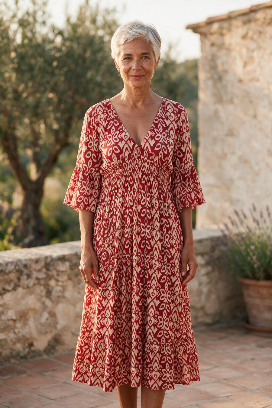Femme de 64 ans portant la robe midi Roseline à imprimé ikat rouge et crème, sur une terrasse ensoleillée du sud de la France