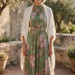 Femme de 66 ans portant la robe longue Héloïse en mousseline verte à fleurs roses, avec un châle crème sur les épaules, sur une terrasse du sud de la France